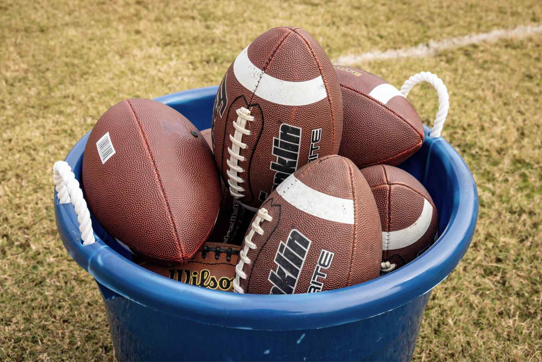 American football balls lying in a bucket.